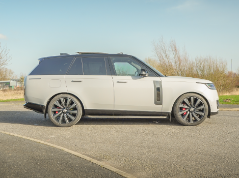 Side view of a white SUV with black and red alloy wheels on a road.