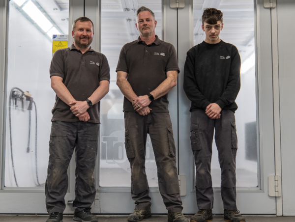 Three men in work uniforms standing in front of a door.
