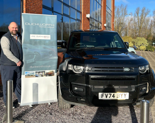 Man standing by a black SUV with a Duckworth Motor Group banner.