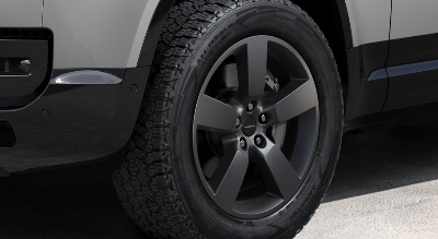 Close-up of a car's front wheel with dark alloy rim and all-terrain tyre.
