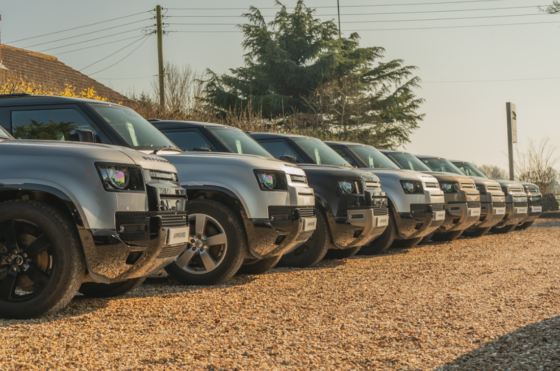 Row of parked Land Rover SUVs on a gravel surface.