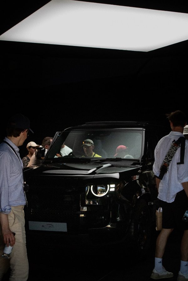 People gathered around a black car with illuminated headlights.