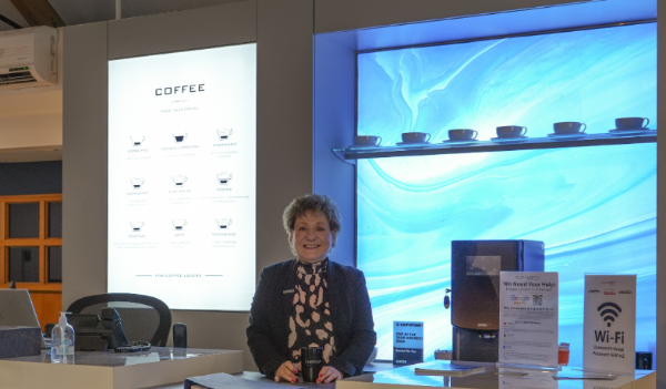 Woman smiling at a coffee station counter with a glowing blue backdrop.