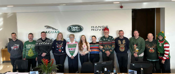 Group of people in Christmas jumpers standing inside a Jaguar Land Rover showroom.
