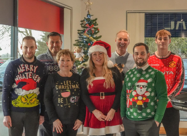 Group of people in Christmas jumpers standing inside a Jaguar Land Rover showroom.
