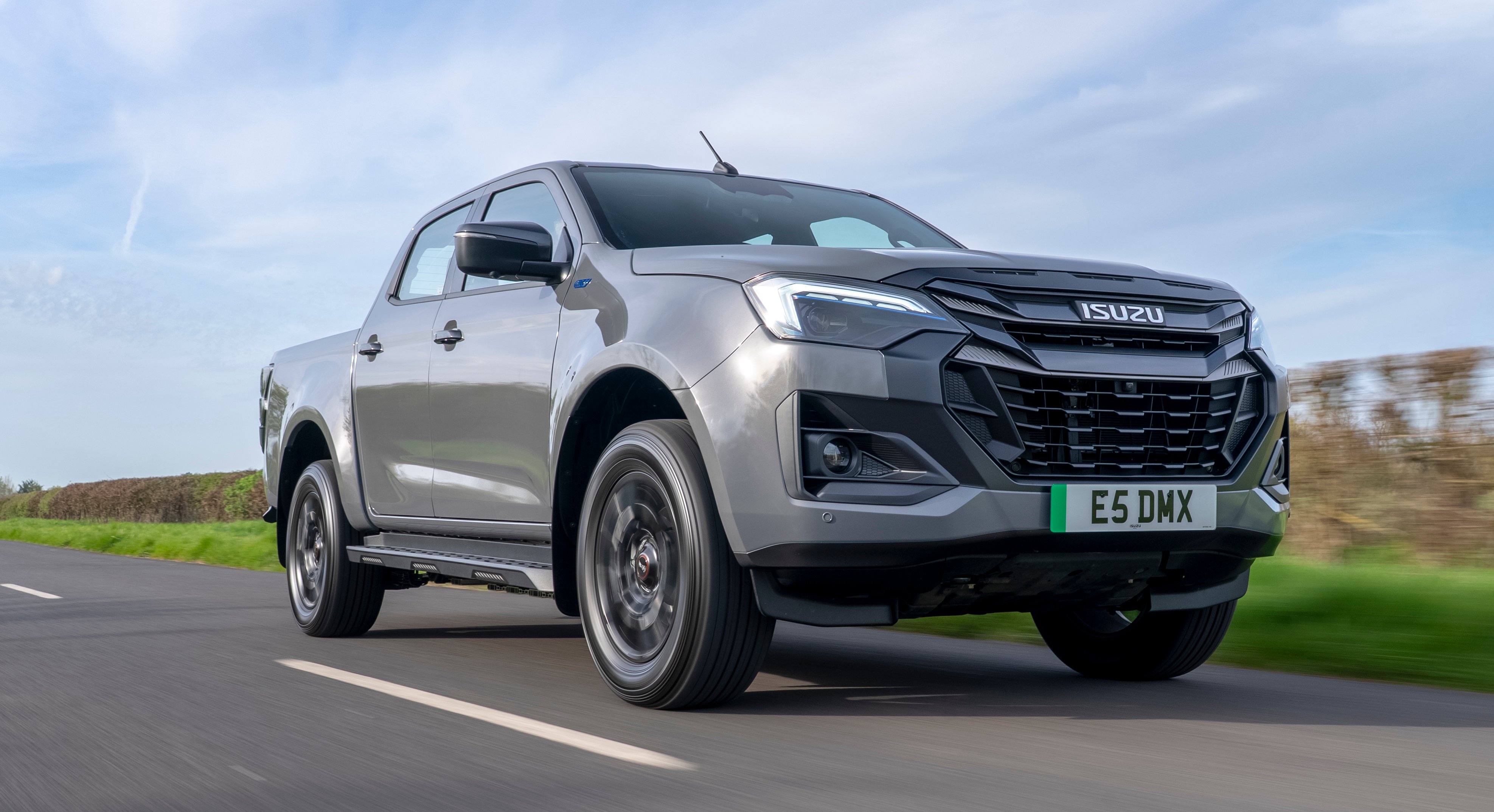 Silver Isuzu pickup truck driving on a road.
