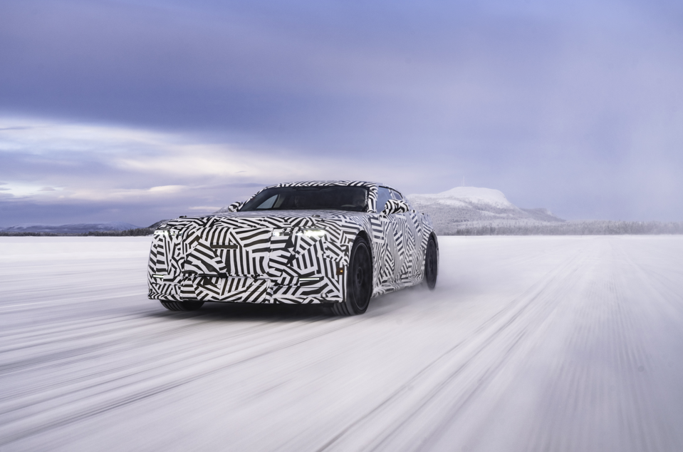 Camouflaged car driving on a snowy landscape with a mountain in the distance.