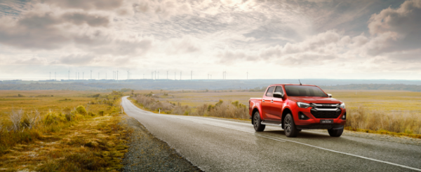 Red pickup truck driving on a rural road with wind turbines on the horizon.