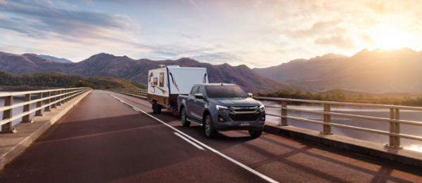 SUV towing a caravan on a bridge with mountains in the background at sunset.