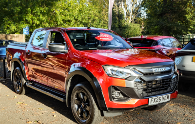 Red Isuzu pickup truck parked on a street with a sale sign on the windscreen.