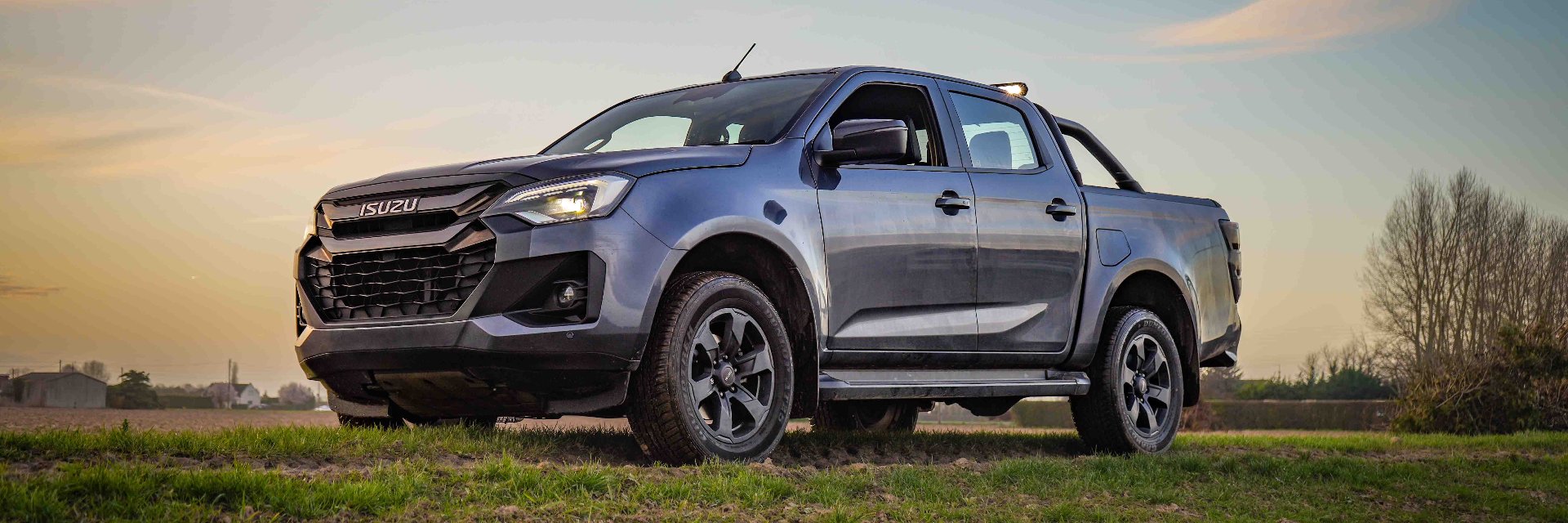 Grey Isuzu pickup truck parked on a grassy field.