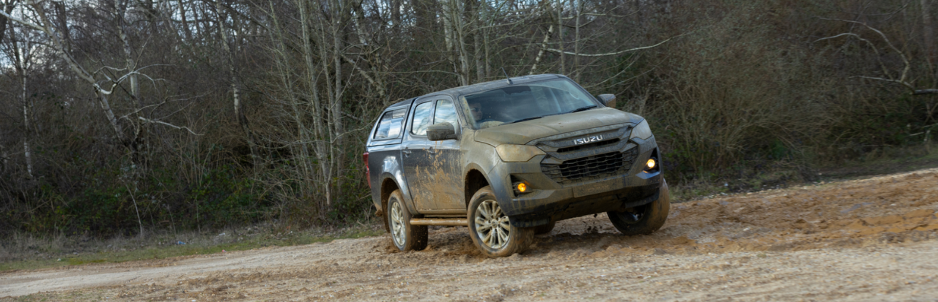 Muddy Isuzu pickup truck driving through a dirt track.