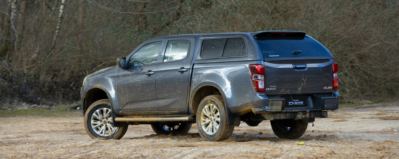 Grey pick-up truck with muddy tyres, parked on a dirt track in a forested area.