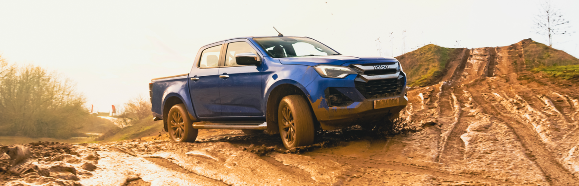 Blue pickup truck driving on a muddy off-road track.