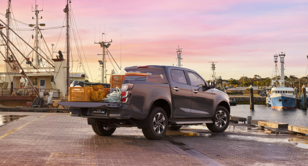 Pickup truck with the tailgate open, parked on a dock with fishing boats.