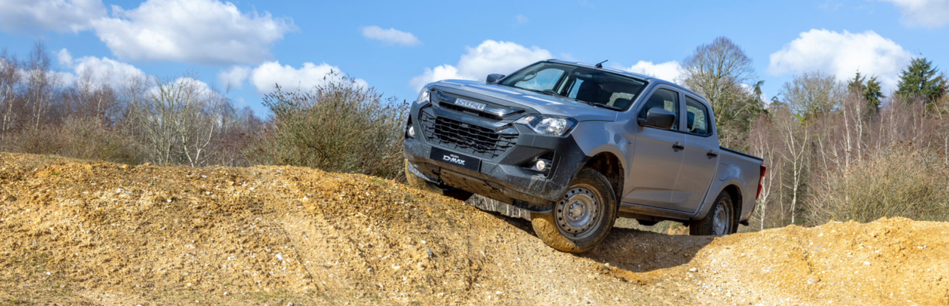 Silver pickup truck navigating a dirt mound near a muddy water pit.