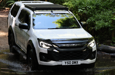 White Isuzu vehicle driving through a shallow water crossing in a forest setting.
