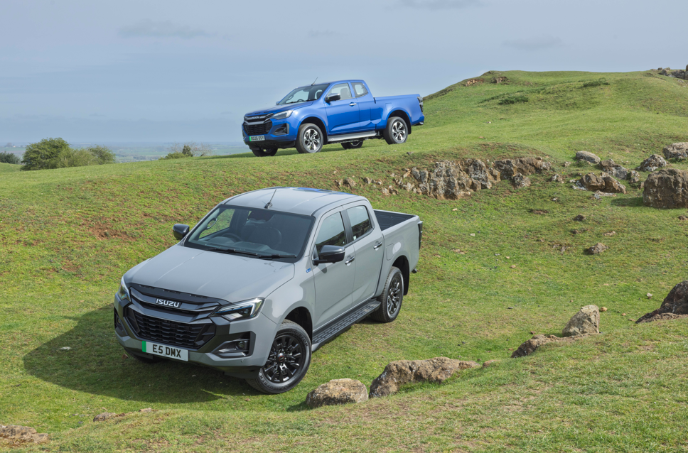Two Isuzu pick-up trucks parked on a grassy, rocky terrain.