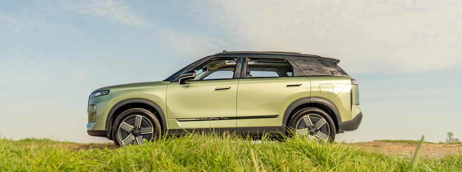 Green SUV parked on grass, side view.