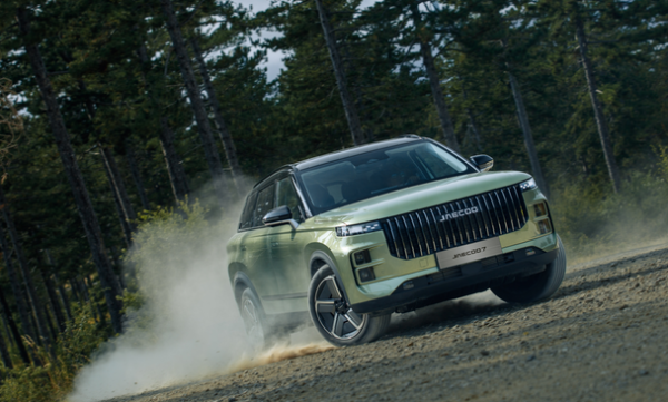 Green SUV driving on a dirt road in a forest setting.