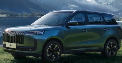 A dark-coloured SUV parked on grass near a lake and mountains.