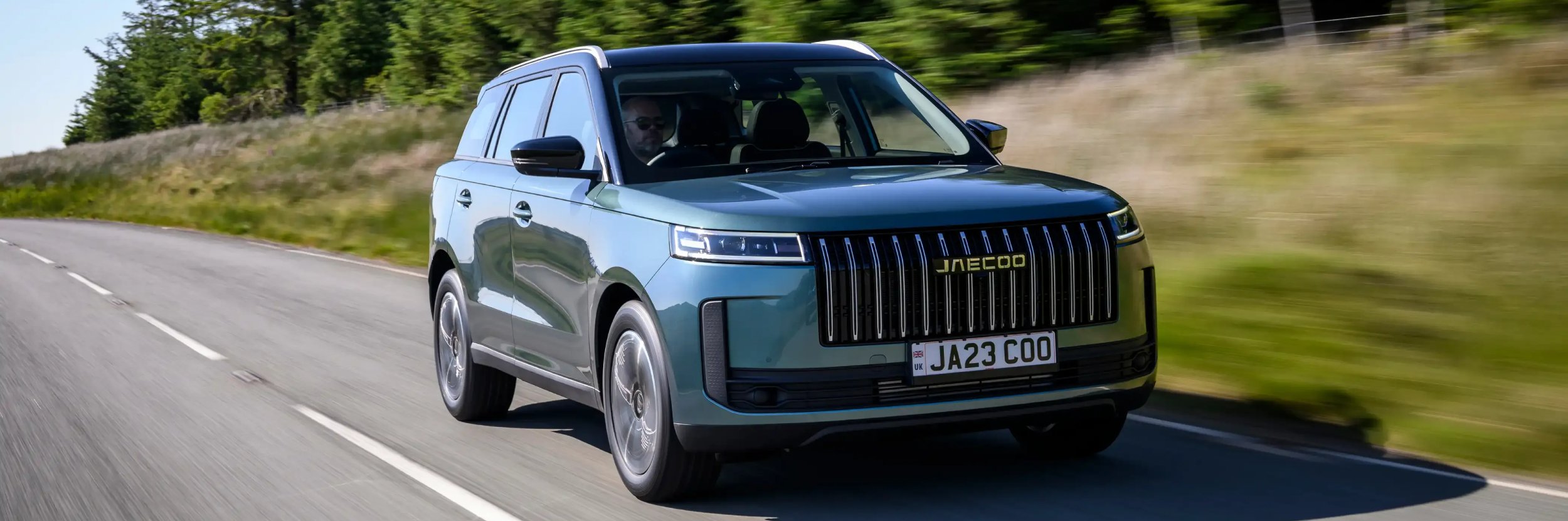 Green SUV driving on a rural road.
