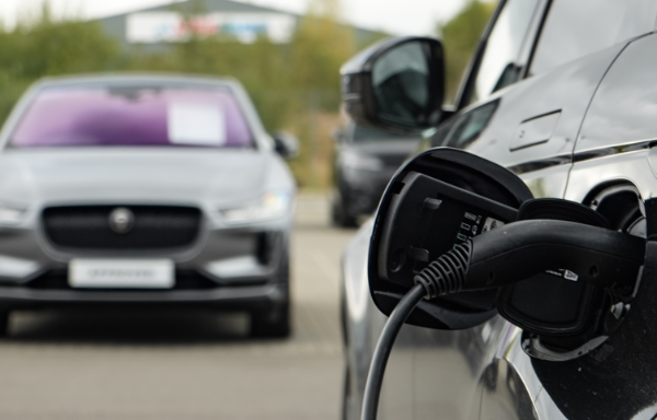 Electric car plugged into a charging station, another car visible in the background.