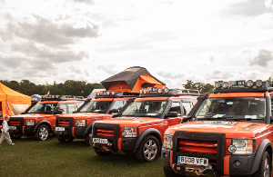 Four orange off-road vehicles parked at an outdoor event with a roof tent deployed.