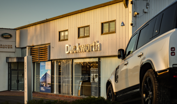 Land Rover dealership exterior with a parked Range Rover Defender in the foreground.