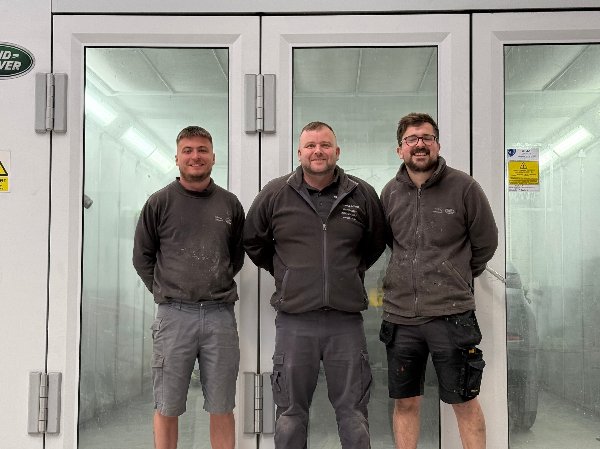 Three men standing in work uniforms, posing for a group photo indoors.