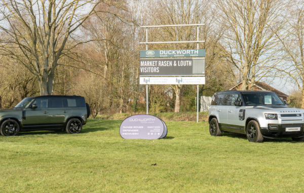 Two Land Rover vehicles parked in front of a dealership sign on grass.