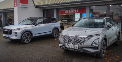 Two cars parked outside a dealership, one silver and one grey.