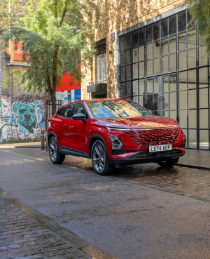 Red car parked on cobblestone street with graffiti-covered walls and pedestrians nearby.