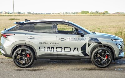 Silver SUV with branding and contact details on the side, parked next to a rural field.
