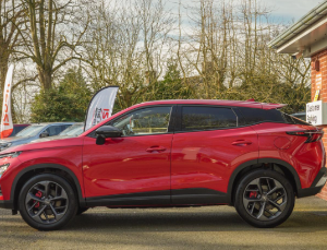 Red SUV parked in profile view outside a building with glass doors.