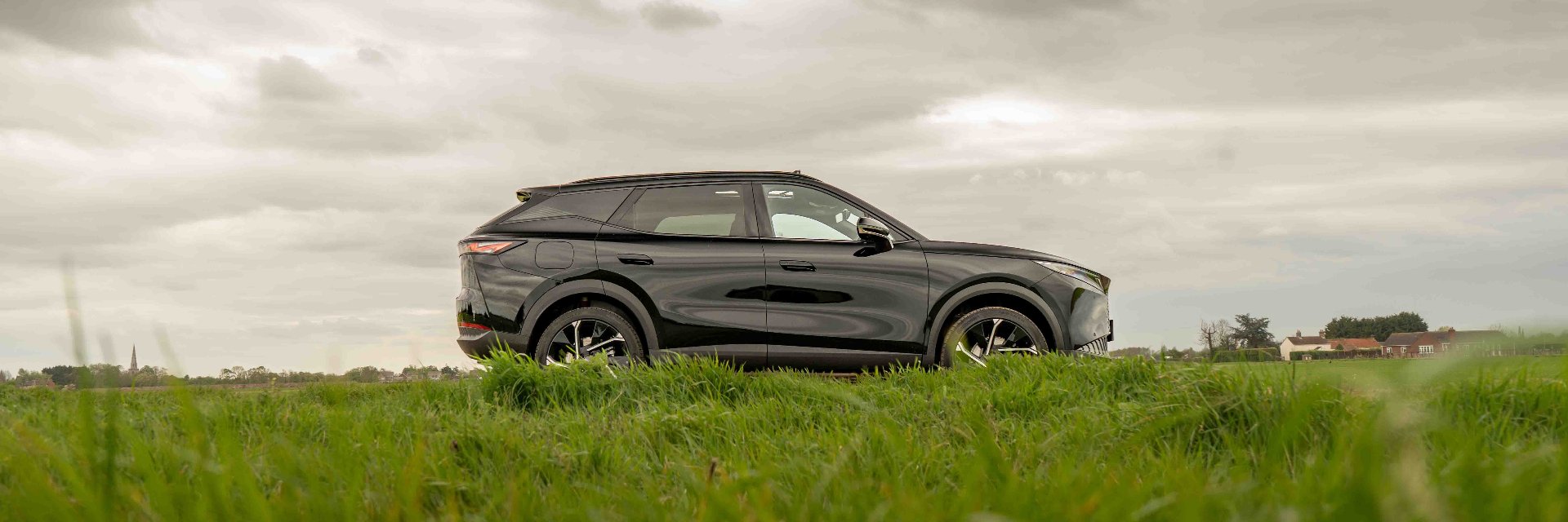 Black SUV parked on grassy field under cloudy sky.