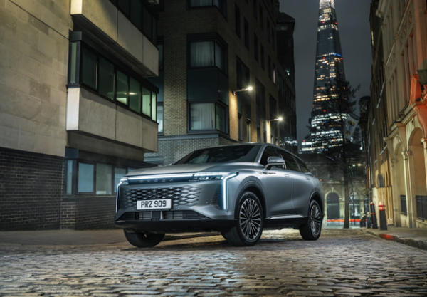 Silver car parked on cobblestone street with tall building in the background at night.