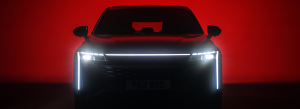 Front view of a black car with illuminated headlights against a red background.