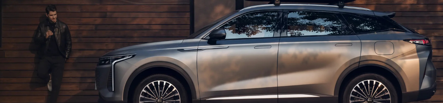 Silver SUV parked, person leaning against wooden wall nearby.