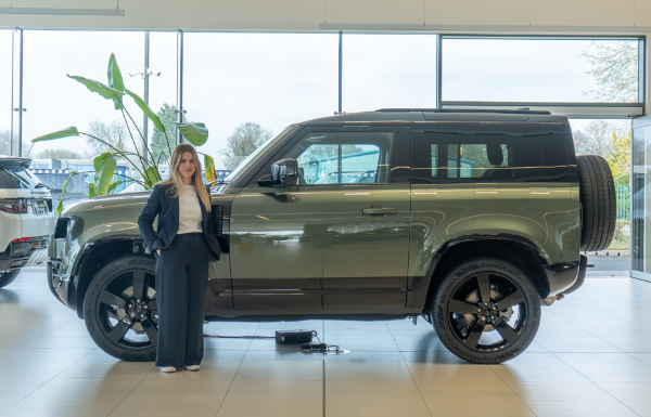 Person standing beside a dark green SUV inside a showroom.