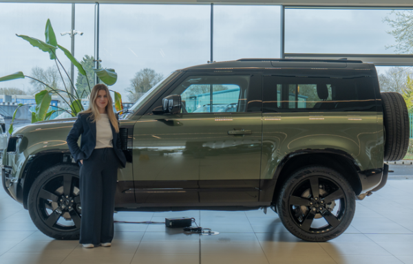 Person standing next to a parked green 4x4 vehicle inside a showroom.