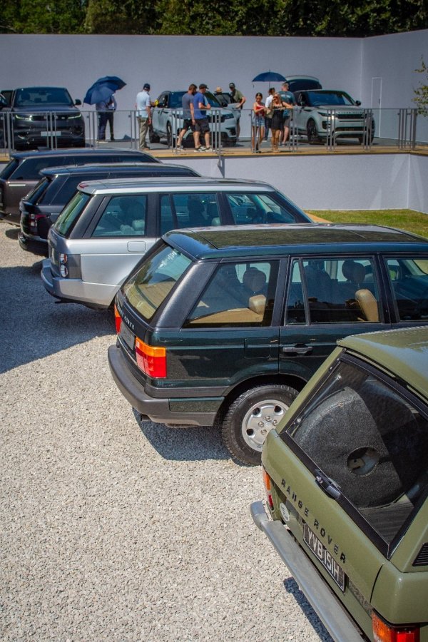 Vintage Range Rovers parked, with people near modern models on a raised platform.
