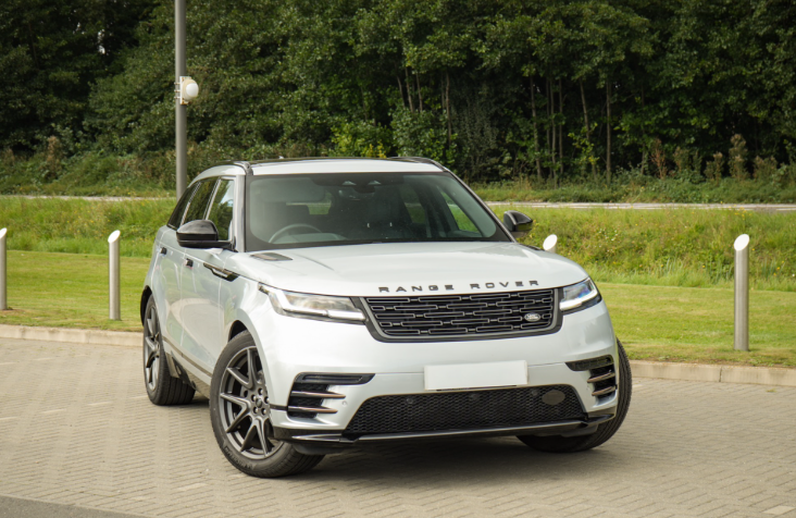Silver Range Rover Velar parked on a paved area with greenery in the background.