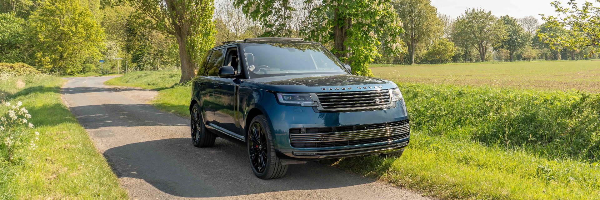 Range Rover parked on a country road near trees and grass.