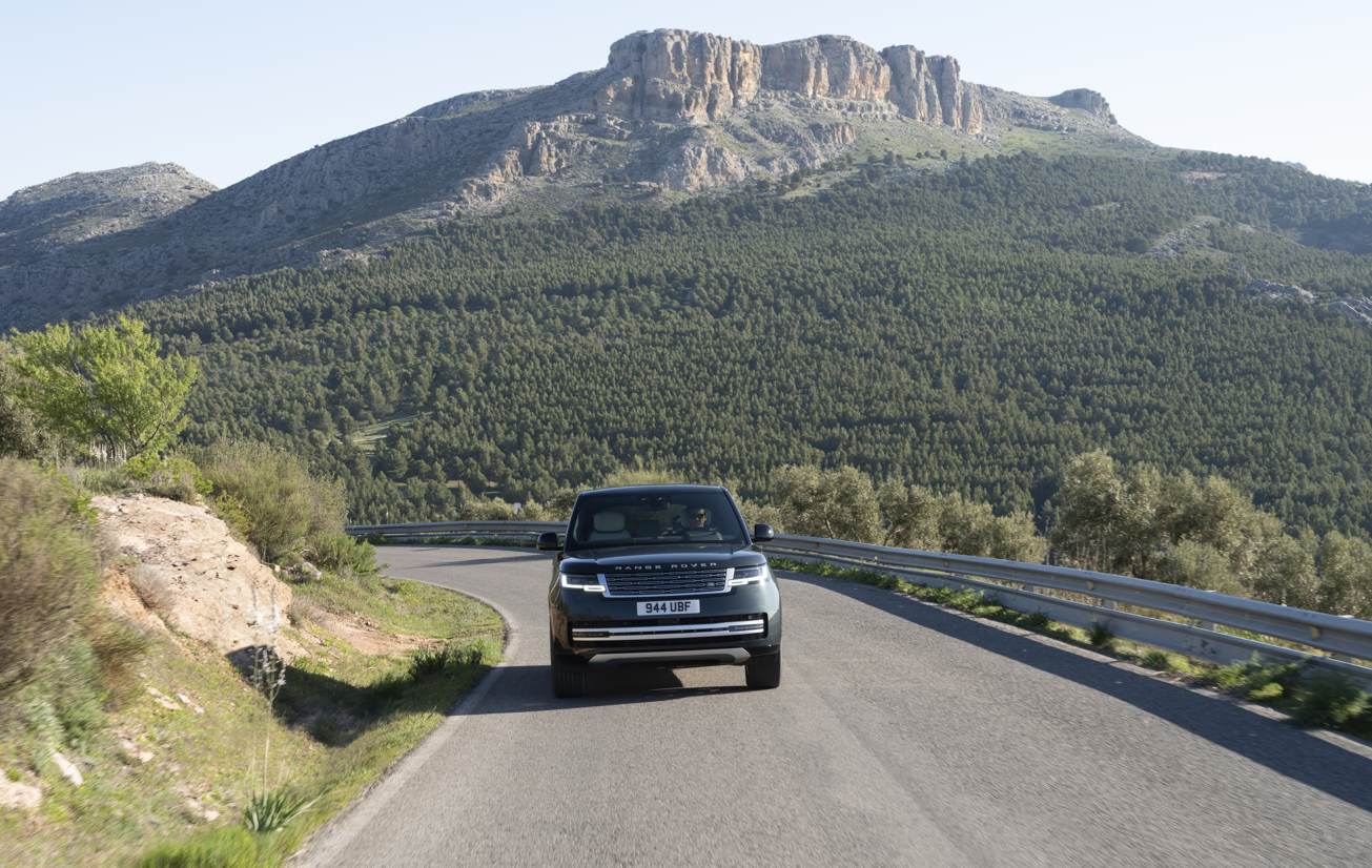 A black Range Rover driving on a mountain road with a rocky hill in the background.
