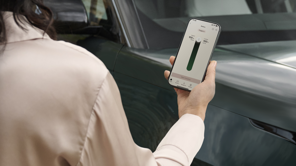 Person holding a smartphone displaying battery status near a car.