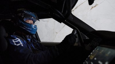 Race car driver in full gear, focused and steering inside a vehicle.