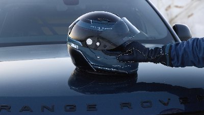 Gloved hand holding a racing helmet on a Range Rover bonnet.