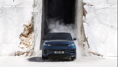 Blue Range Rover car driving through a marble quarry opening with dust around it.
