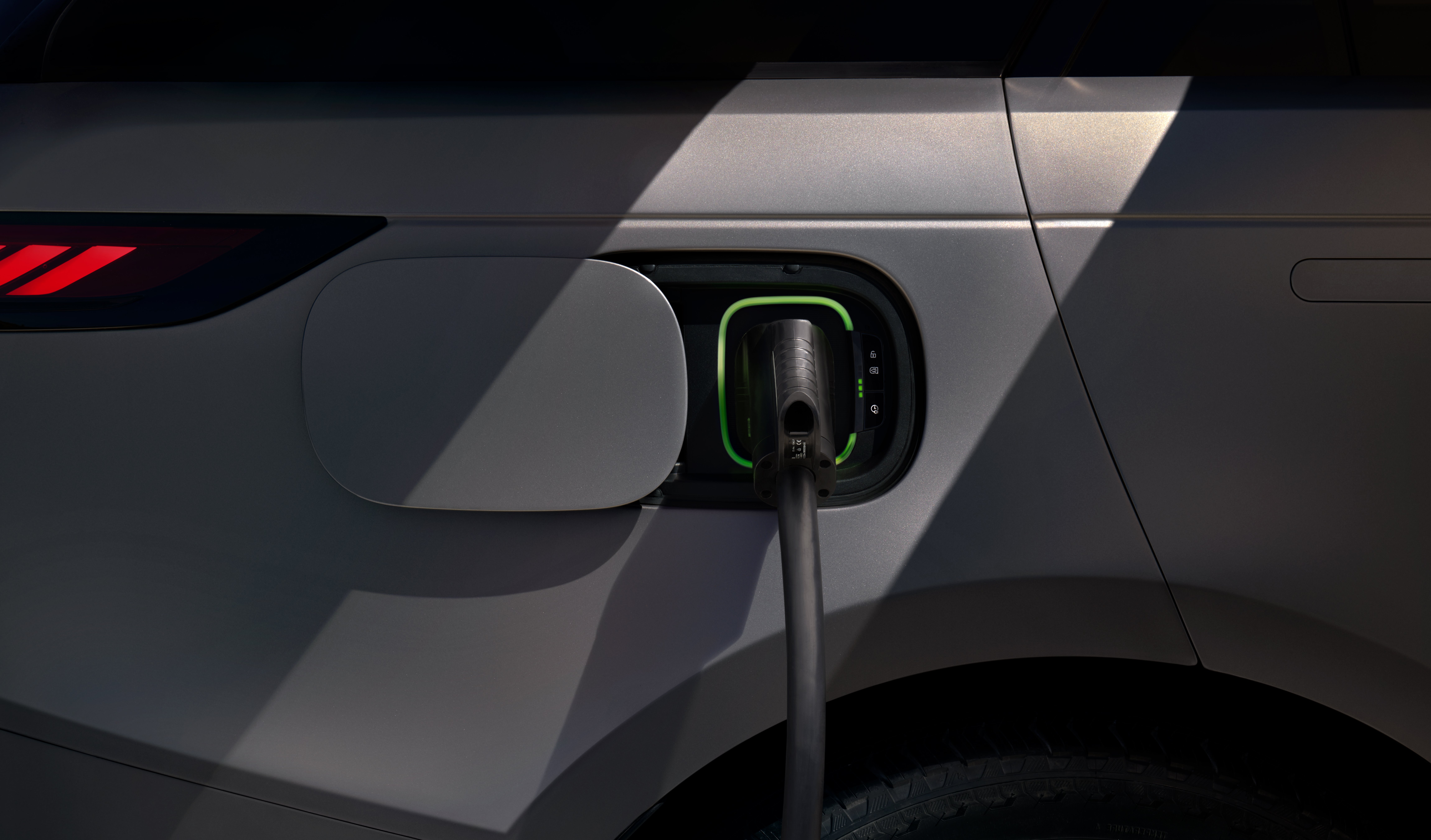 Electric vehicle being charged via a plug-in point on its rear side.